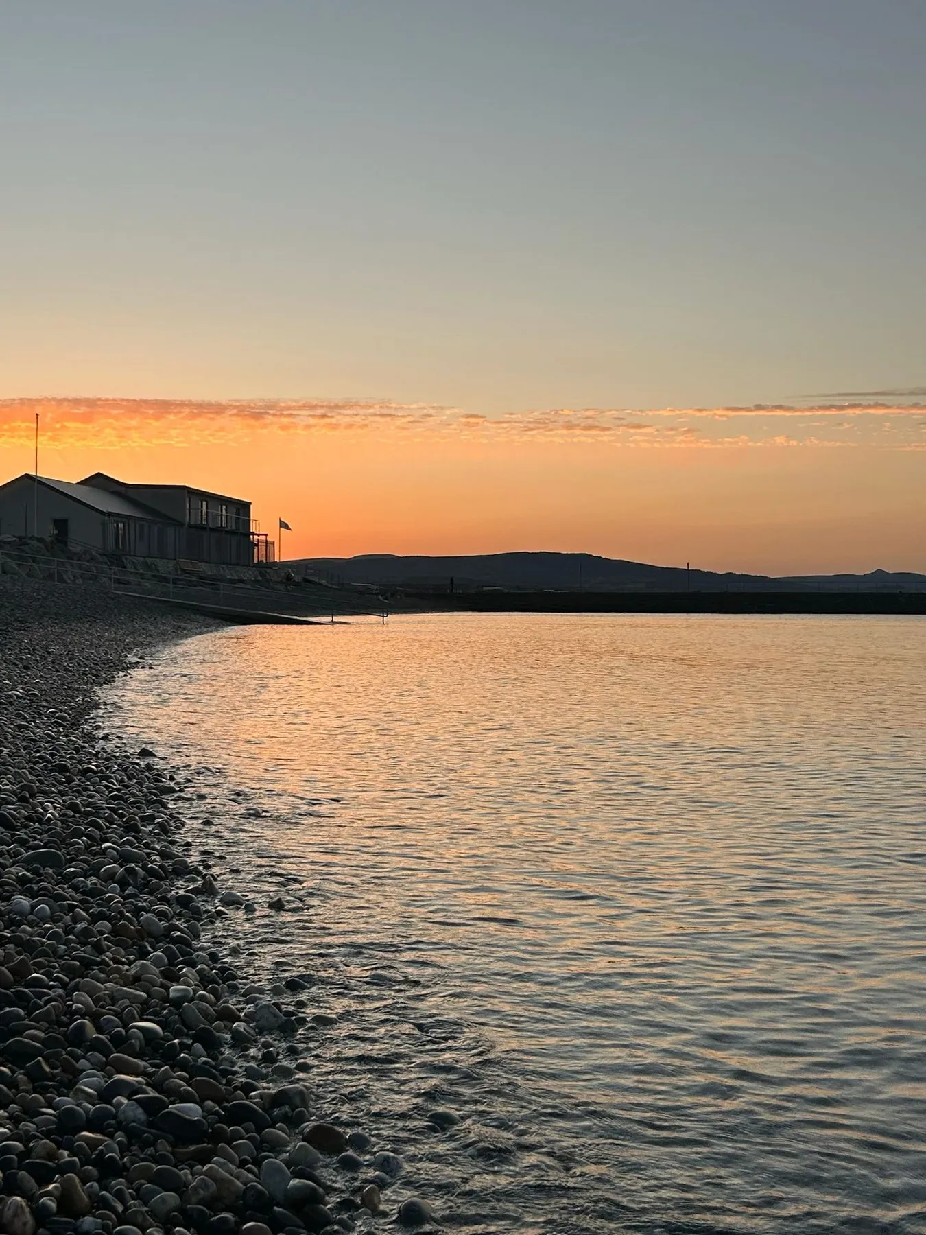 Sunset over the cobble beach with the sauna building on the shore