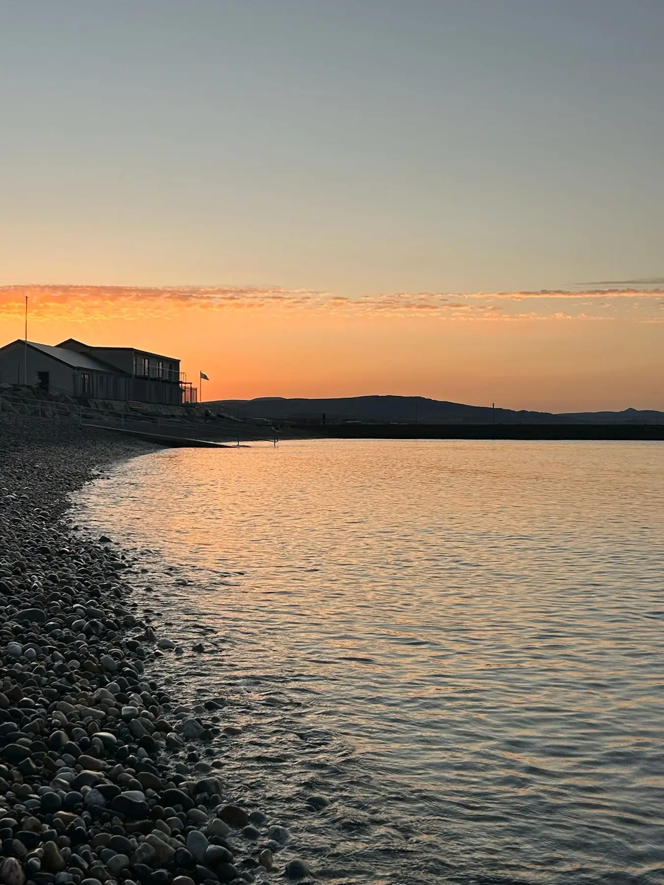 Sunset over the cobble beach with the sauna building on the shore
