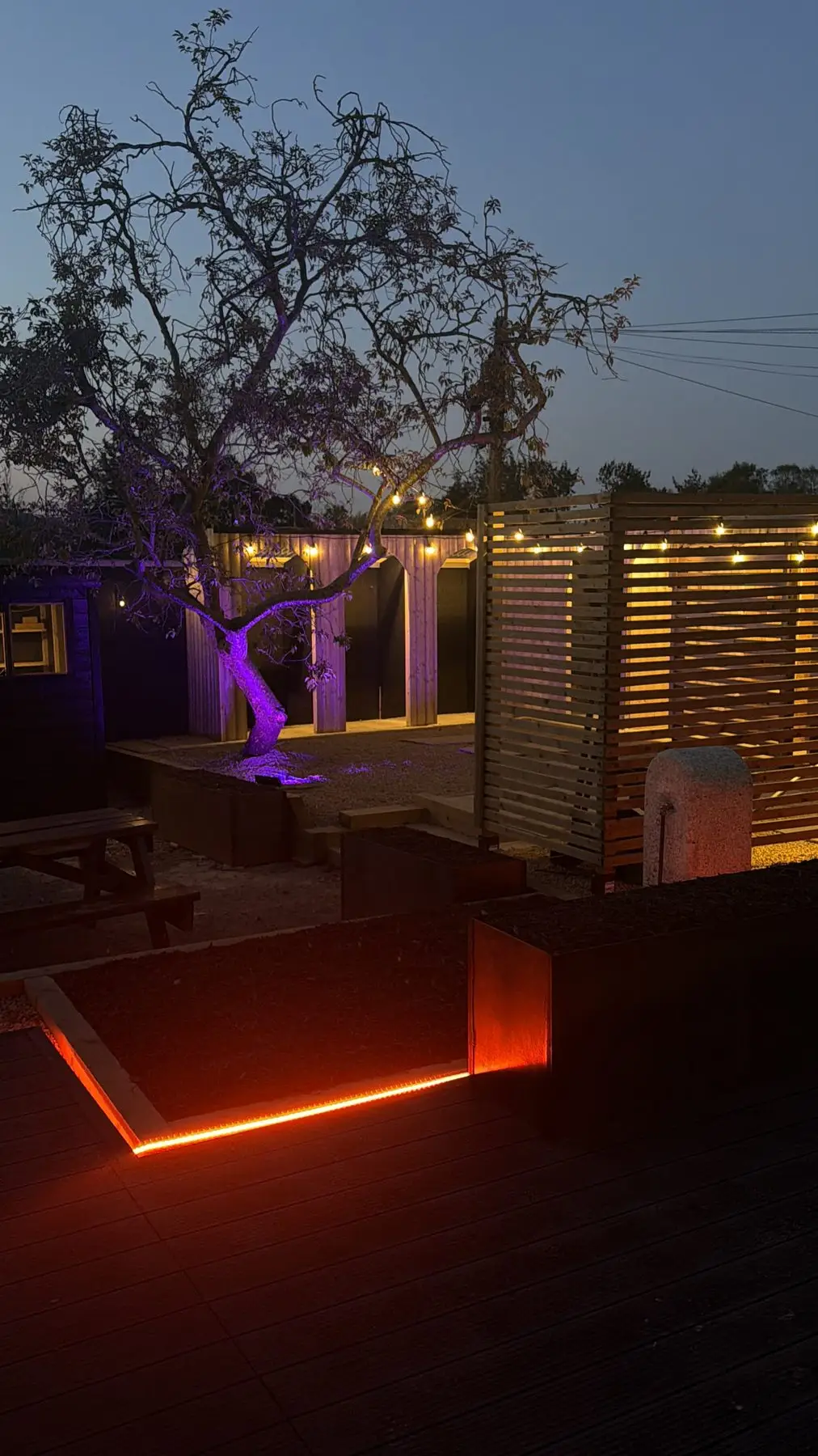 The sauna courtyard at dusk, festoon lights glowing over the cold plunge