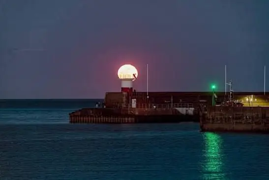 A full moon rising behind the pier lighthouse at night