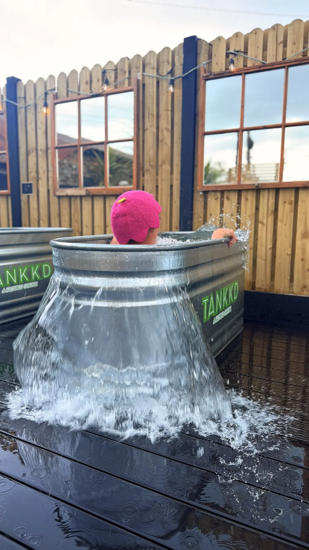 A woman in a pink swim cap splashing in the cold-plunge tank