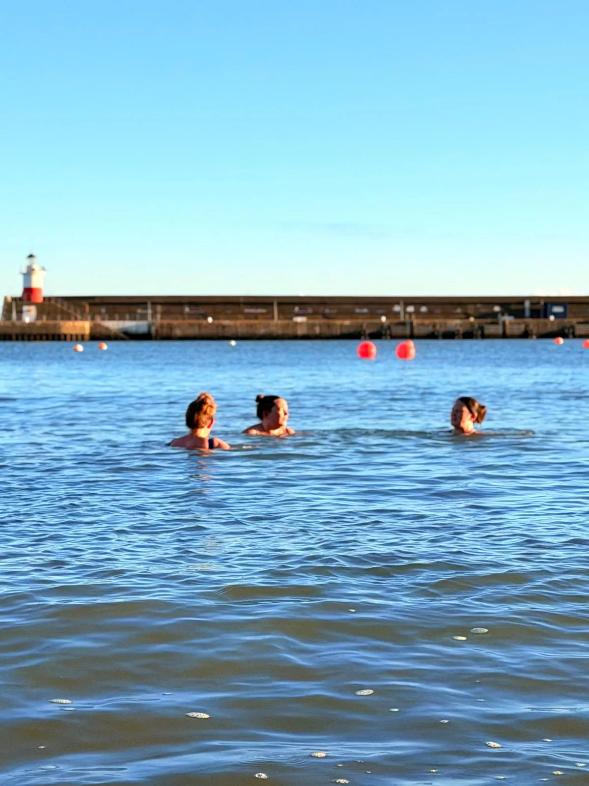 Three friends sea-swimming together by the harbour wall and lighthouse