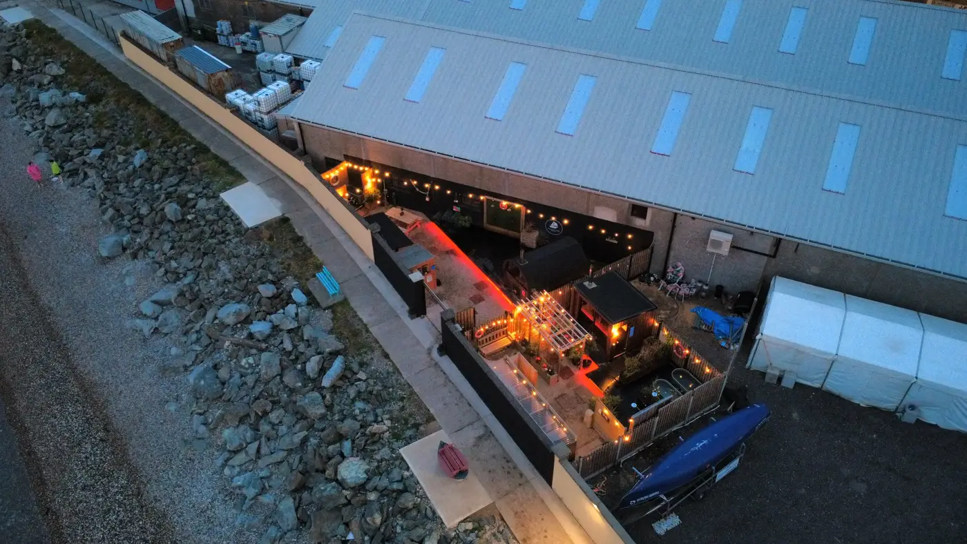 Aerial view at dusk of The Boat Yard Sauna in Wicklow, festoon lights glowing beside the slipway and sea